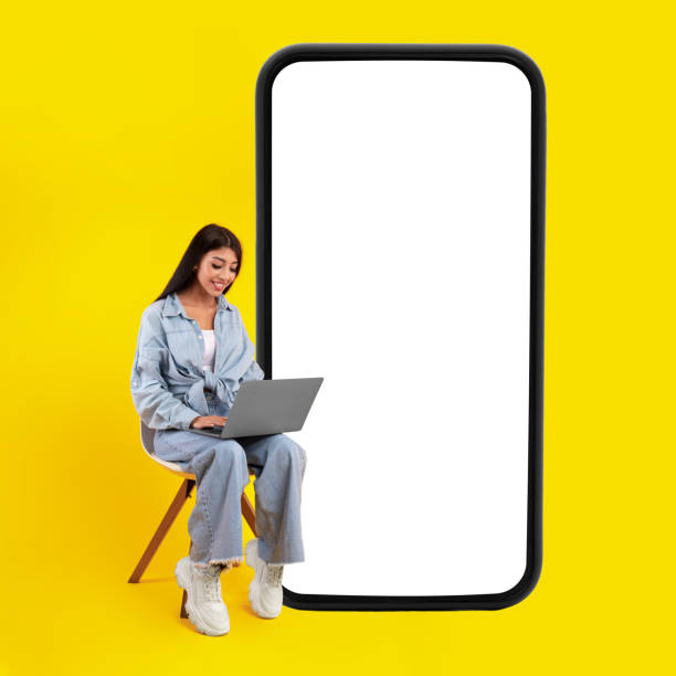 istock Happy lady using pc sitting near big mobile phone screen 1384839523