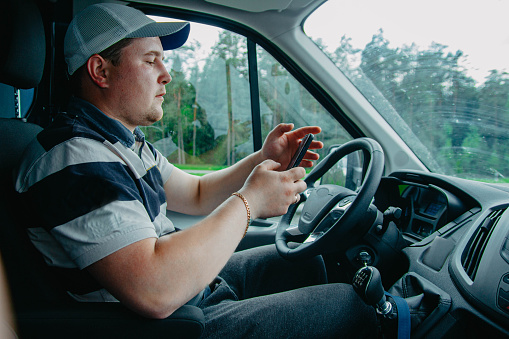 male truck driver uses smartphone while sitting in cab.
