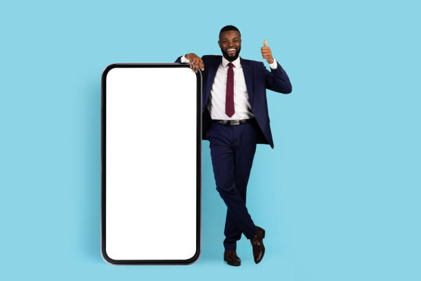 business app. cheerful african american businessman standing near big blank smartphone - thumbs up business people isolated imagens e fotografias de stock