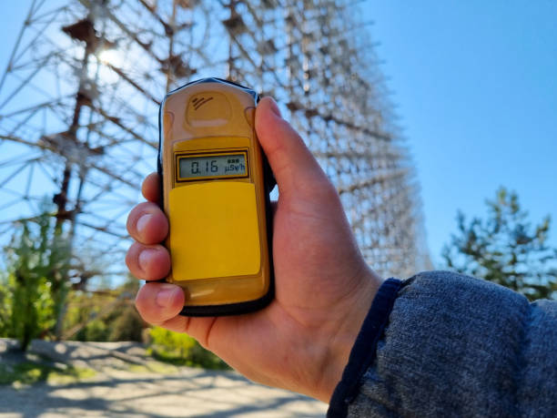 Hand holding a yellow dosimeter indicating radiation on the screen. Enormous Duga radar complex in the background. Warm summer day, nice paralel lines Hand holding a yellow dosimeter indicating radiation on the screen. Enormous Duga radar complex in the background. Warm summer day, nice paralel lines radiation dosimeter stock pictures, royalty-free photos & images