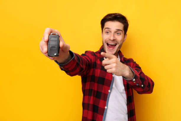 istock Excited Man Holding Car Key And Pointing, Yellow Background 1384846497