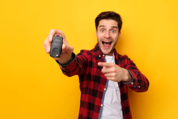 istock Excited Man Holding Car Key And Pointing, Yellow Background 1384847019