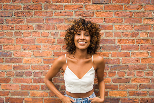 Afro-american woman portrait on a brick wall, playful and beautiful female with positive mood
