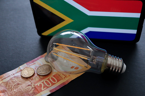 Concept picture of rolling blackouts or loadshedding in South Africa implemented by Eskom. South African currency and the South African flag in the background