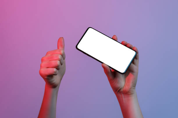 istock A phone with a white, blank screen in a woman's hand on a neon gradient background. Other hand showing like sign. 1384858242