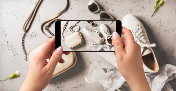 Woman taking photo of spring fashion accessories with smartphone. Influencer and social media. Woman taking photo of white leather sneakers shoes, handbag and sunglasses with smartphone. Blogger, influencer or stylist capturing spring fashion accessories for social media. Grey background. second hand stock pictures, royalty-free photos & images