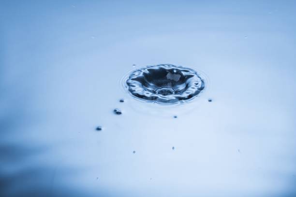 istock Close up view of falling drops on blue water surface isolated on background. 1384864916