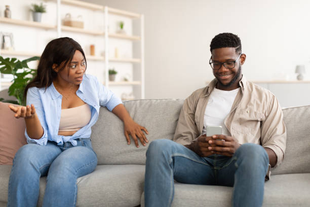 mujer infeliz y enojada mirando a su hombre usando el teléfono - african descent addiction african ethnicity rudeness fotografías e imágenes de stock