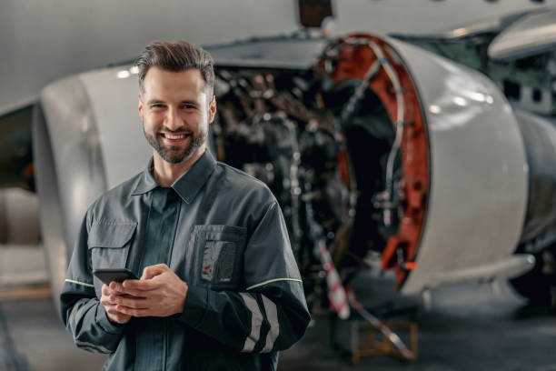 格納庫で携帯電話を使用して陽気な航空会社のメカニック - telecommunications equipment technician repairing engineer ストックフォトと画像