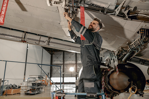 Smiling bearded man maintenance technician using wrench tool while repairing airplane in hangar