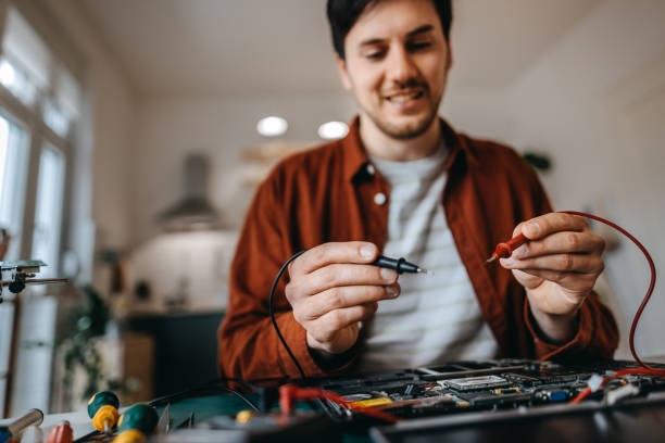 mittelteil des jungen mannes, der die muttertafel mit multimeter auf dem tisch untersucht - holding screwdriver stock-fotos und bilder