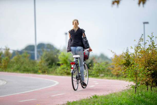 Young Woman Riding Her Bicycle Uphill on Bicycle Lane Through Public Park stock photo