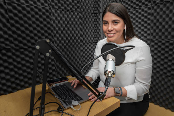 ritratto di una donna sorridente durante la registrazione di un podcast in una cabina audio, rivestita con isolamento acustico - mid adult audio foto e immagini stock