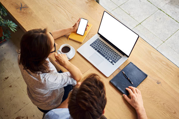 Overhead picture of two people looking at blank laptop  and smartphone screen sitting at cafe stock photo
