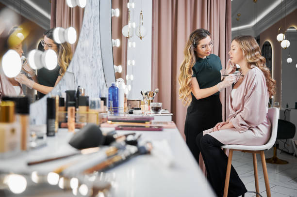 istock Woman makeup artist doing makeup on client in beauty salon. 1384890634