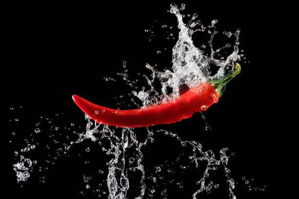 istock Red pepper with water splash over black background 1384891012