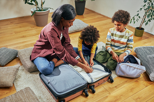 African woman and her two children packing their clothes into a suitcase, getting ready for a trip.