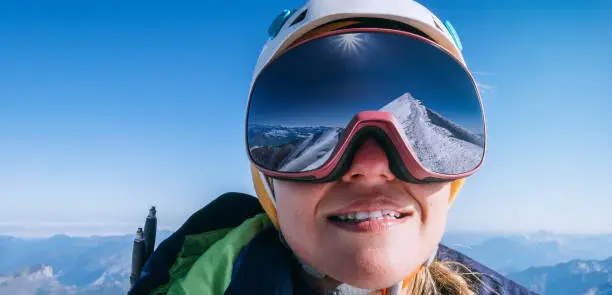 High altitude mountaineer smiling female portrait in safe ski helmet and goggles on the Mont Blanc 4810m with picturesque Alpine mountains background. Active sporty people and success concept image