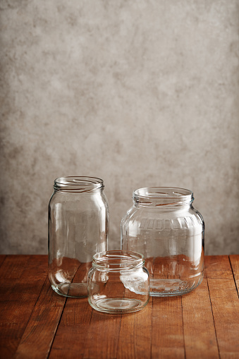 Variety of empty clear glass jars on wooden table against concrete wall