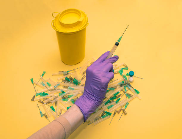 Hand with medical needels Female hand in protective latex glove holding syringe over used pile of infectious needles needels stock pictures, royalty-free photos & images