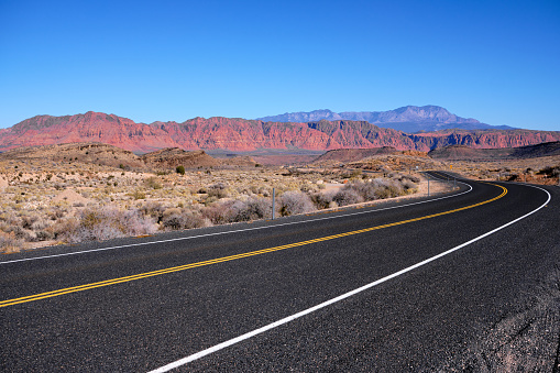 Driving on the smooth, black pavement of old Highway 91 in South Western Utah. On the horizon is Red Rock country under cloudless, blue skies