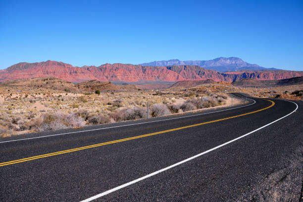 On The Road Again - Driving to Utah's Red Rocks Driving on the smooth, black pavement of old Highway 91 in South Western Utah. On the horizon is Red Rock country under cloudless, blue skies empty road stock pictures, royalty-free photos & images
