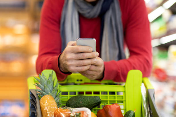 istock Cropped of man using cell phone while shopping at supermarket 1384900534
