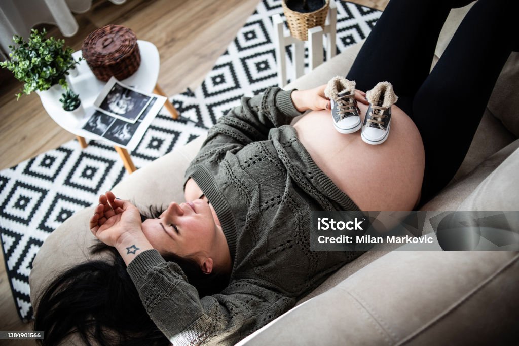 You will be a modern baby, I am waiting for you to give you love A pregnant young woman is lying on the bed and holding small baby sneakers on her stomach Baby - Human Age Stock Photo
