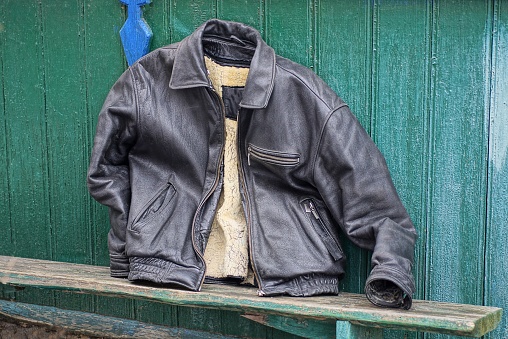 old black leather jacket with a gray wool lining lies near the green wooden wall on the street