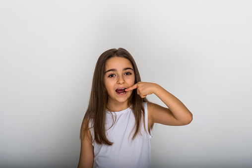 Young girl  grey background smiling confident showing and pointing with fingers teeth and mouth. Health concept.