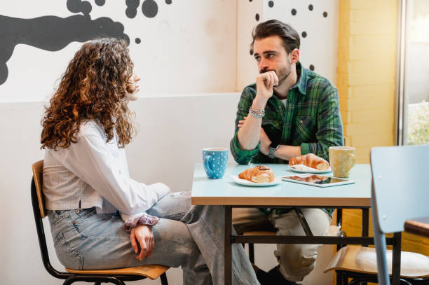 pareja joven sentada a la mesa en un café hablando con caras serias. - coffee buzz fotografías e imágenes de stock