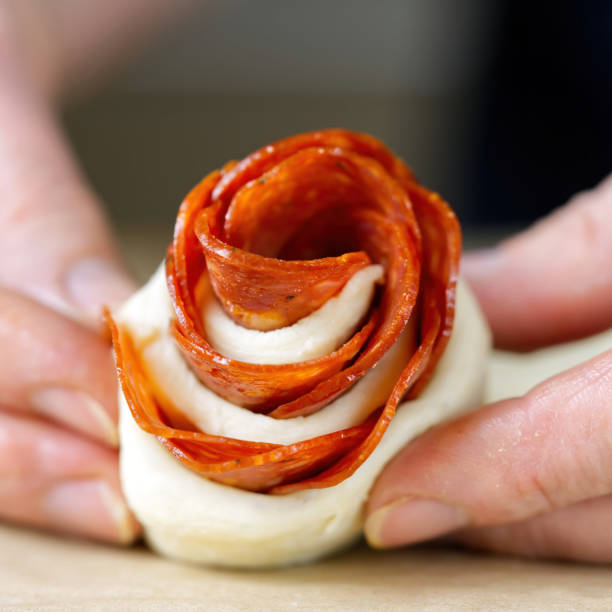 woman is making rose-shaped pepperoni snack. pastry with salami. homemade puff pastry ready to bake - appetizer people marinara cheese imagens e fotografias de stock