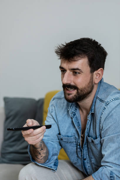 istock Handsome young man holding a TV remote while watching television in the morning 1384943676