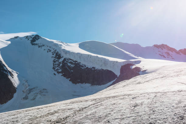 Sun rises over snowcapped mountain and blue sky, Saas Fee