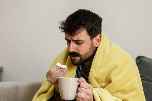 istock Young man blowing his nose and drinking hot tea 1384950901
