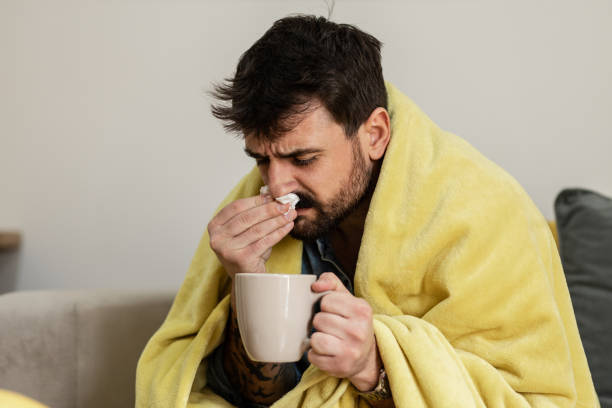 istock Young man wiping his nose and drinking hot tea 1384951045