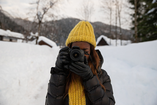 A photographer takes a picture while standing in a mountain scenery in the cold with snow
