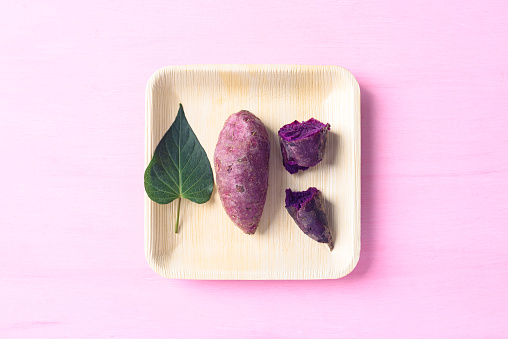 Purple sweet potatoes on natural plate with pink background, Table top view