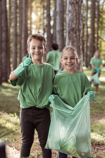 Girl and boy showing thumbs up while cleaning forest from garbage