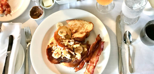 A breakfast table setting of french toast, bacon, fruit and juice A table of breakfast foods includes french toast, bacon, fruit and juice on a crisp white tablecloth french toast bacon bread butter stock pictures, royalty-free photos & images