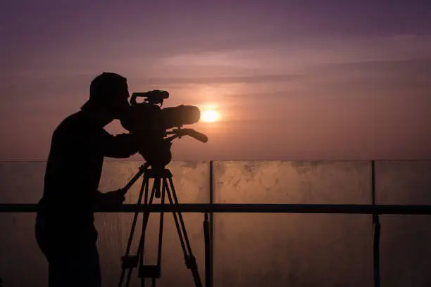 The silhouette of a camera operator in front of a dramatic sunset.