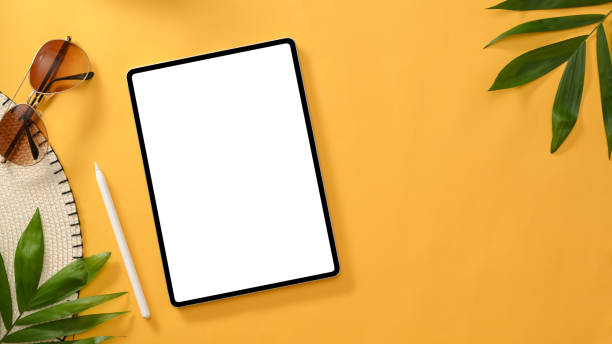 Digital tablet touchpad white screen mockup, stylus pen, sunglasses, beach hat, palm tree and copy space on yellow background. top view