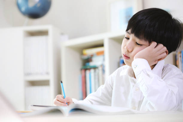 Tired student tired of tedious study and a lot of piled up school homework A student exhausted from the piled up of school homework and tedious study is learning by solving difficult problems with a tired look. asian kids learning stock pictures, royalty-free photos & images