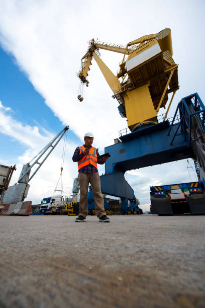 istock Engineers and crane.smiling dock worker holding radio and Container ship under bridge crane in port background. 1384982536