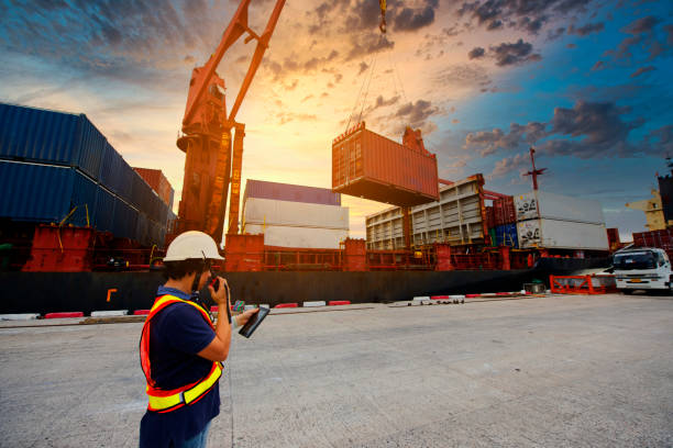 istock Engineers and crane.smiling dock worker holding radio and Container ship under bridge crane in port background. 1384982537