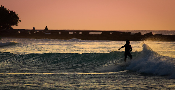 A silhouetted surfer rides a turquoise wave at sunset