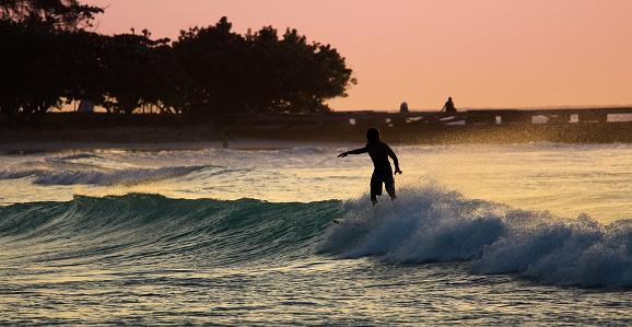 A silhouetted surfer rides a turquoise wave at sunset