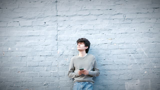4k video footage of a young man using a smartphone while leaning against a grey wall