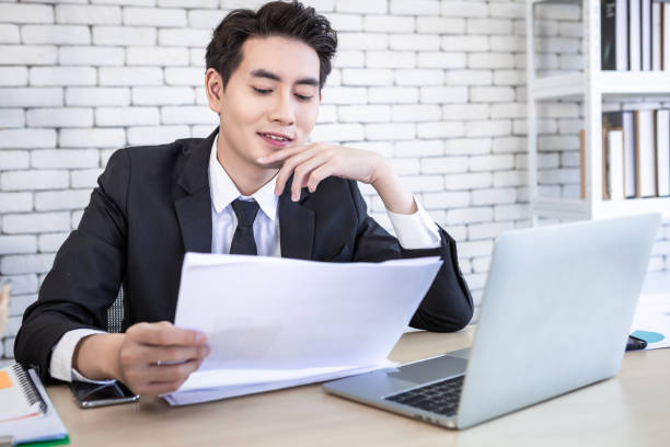 istock asian young businessman have stressed see a the document  business plan and laptop computer on wooden table after business losses In the office room background. 1384989739