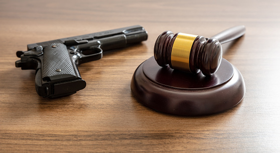 Crime, gun carry and use punishment concept. Judge gavel and handgun on lawyer office desk. Wooden courthouse table, close up view